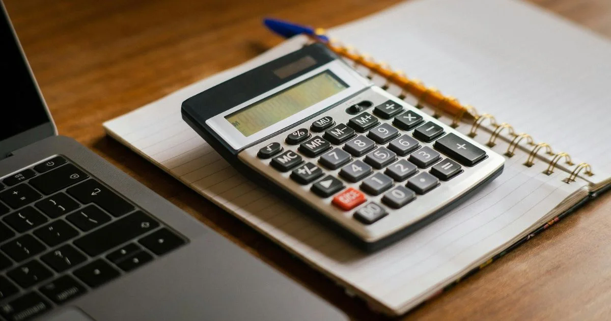 Calculator and notebook beside laptop on desk.