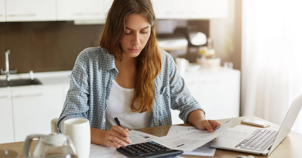 Woman calculating household expenses at kitchen table.